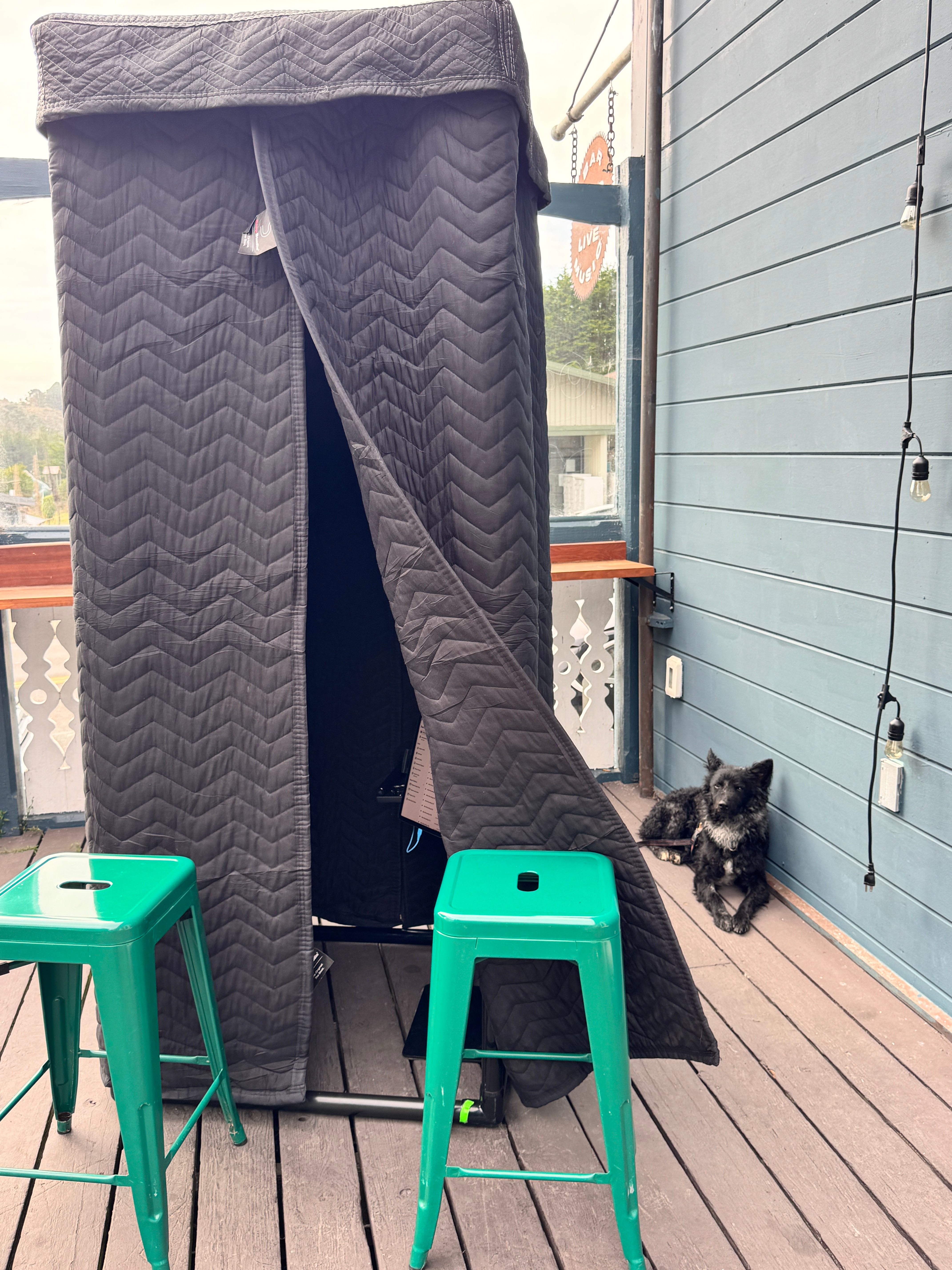 Step-In! booth on a deck with green stools, curtain parted, a small dog nearby
