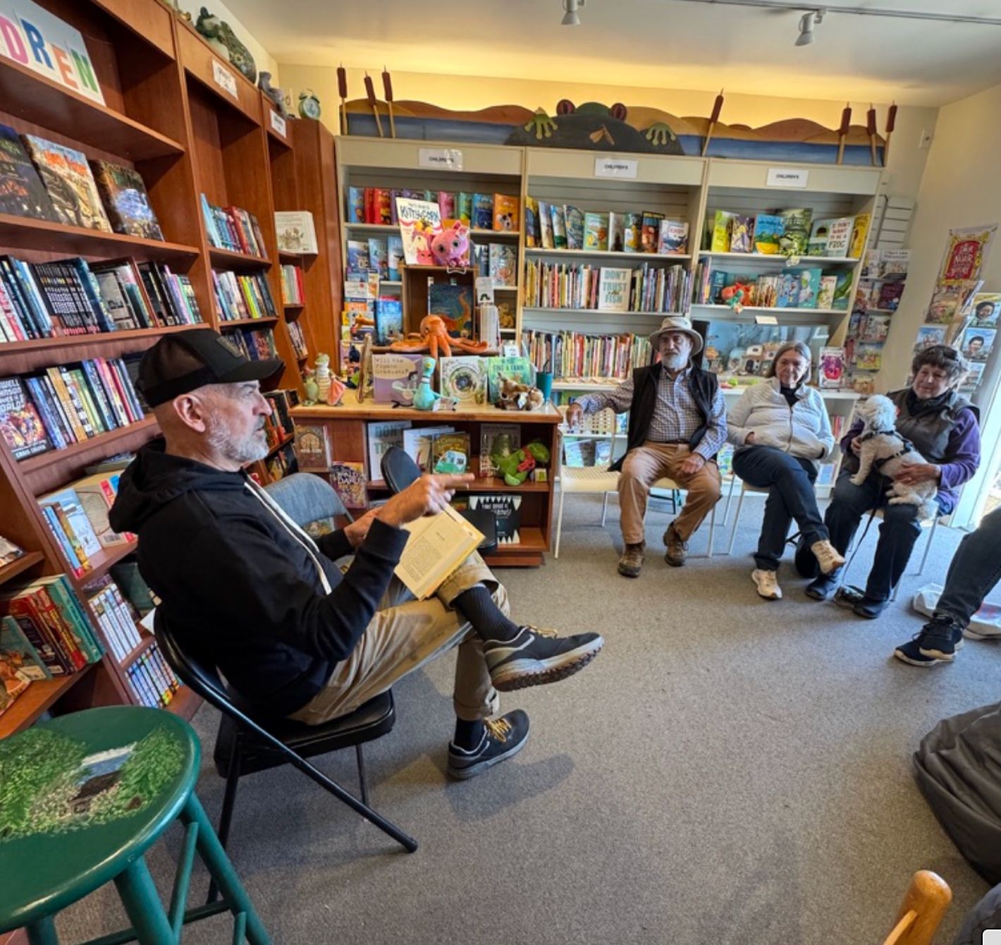 A group gathered in a bookstore, one person reading aloud while others listen